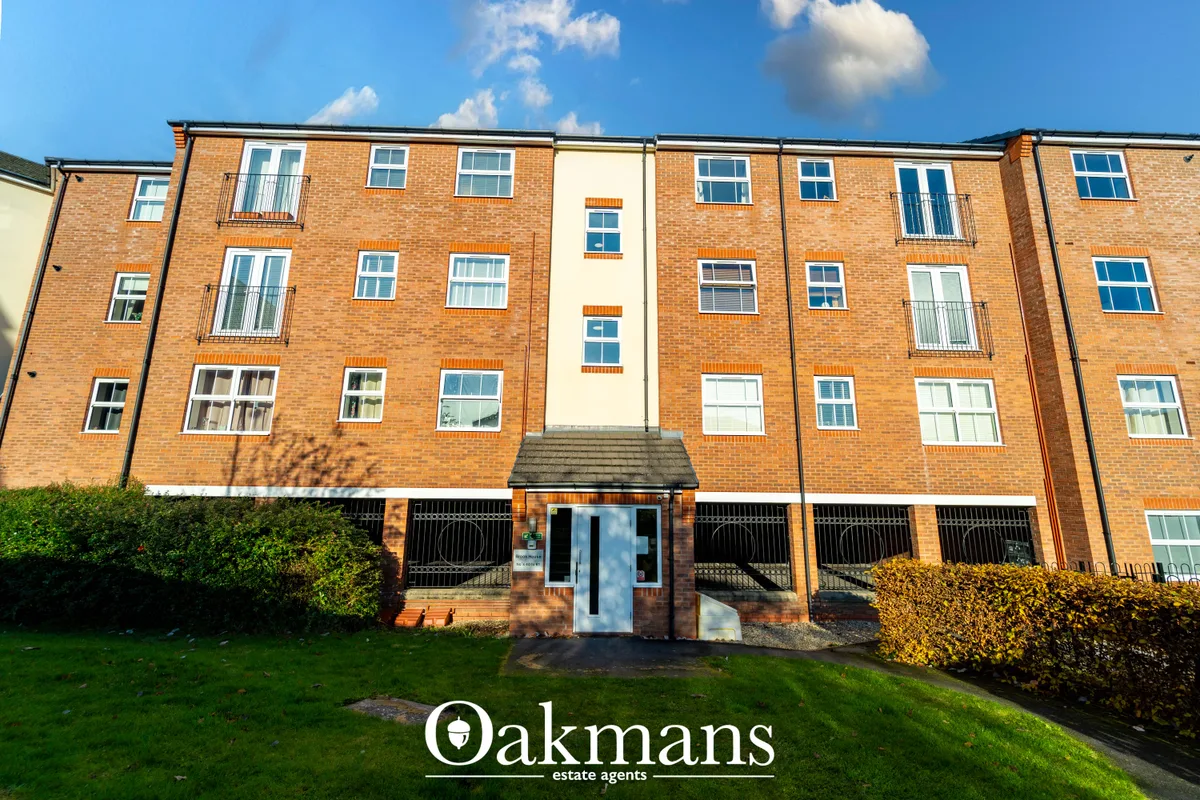 Modern brick apartment building with blue-framed windows, central entrance with steps, landscaped front garden and clear