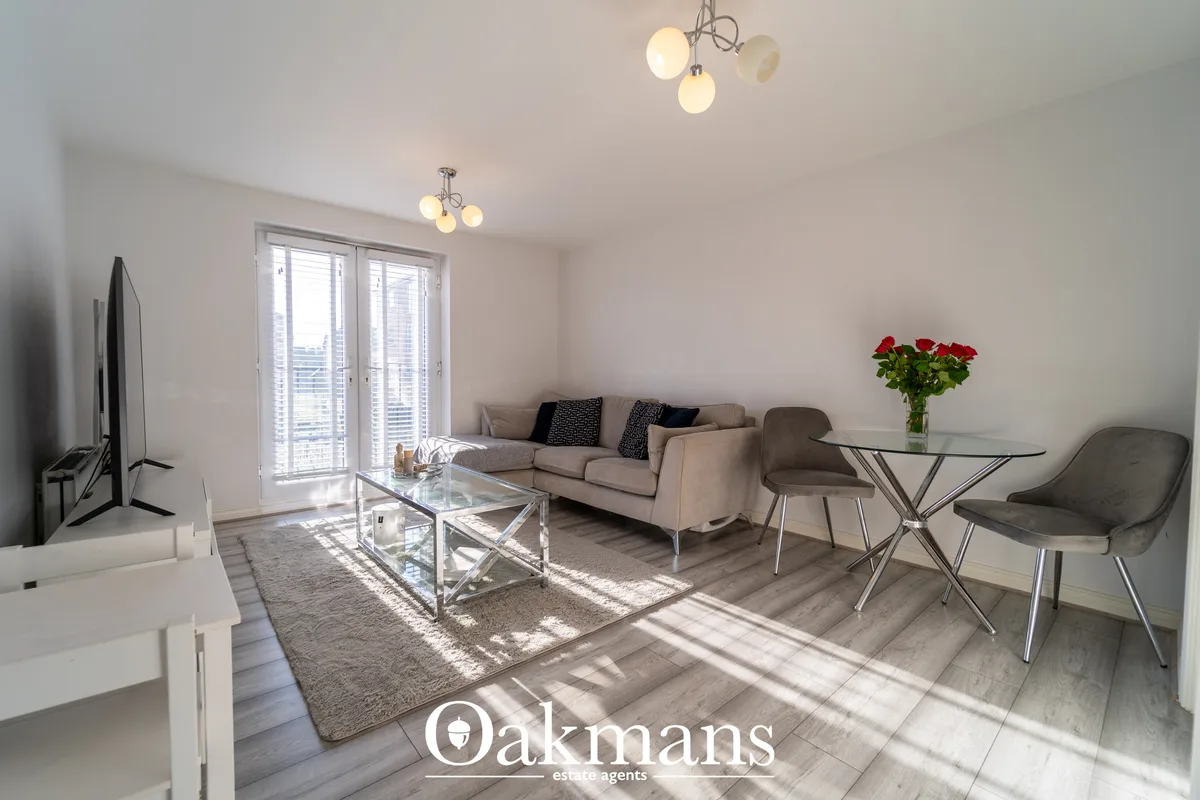 Bright modern living room with beige sofa, glass coffee table, dining area with fresh roses, pendant lights, and floor-t