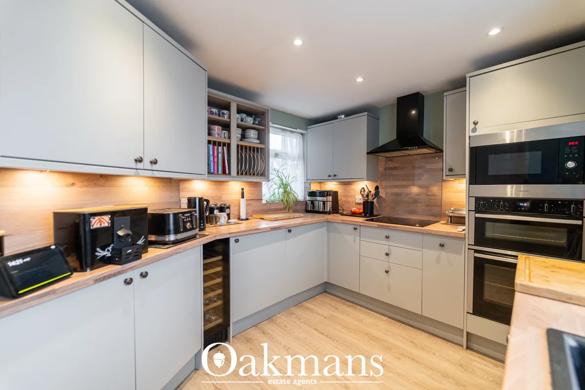 Modern fitted kitchen with white cabinetry, wooden worktops, black appliances, warm under-cabinet lighting, and breakfas