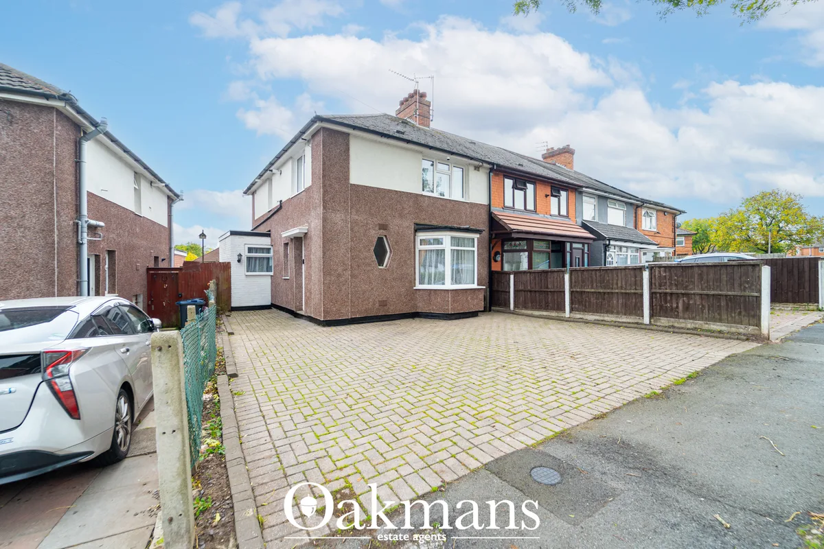 Semi-detached brick and rendered house with driveway, paved forecourt, wooden fence, parked car and clear sky