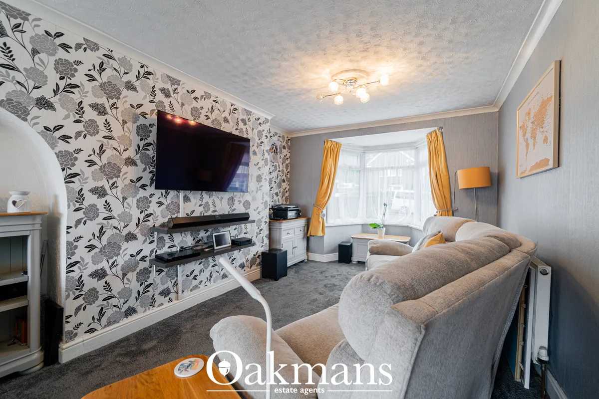 Spacious living room with floral wallpaper, wall-mounted TV, grey upholstered sofa, fireplace, bay window with gold curt
