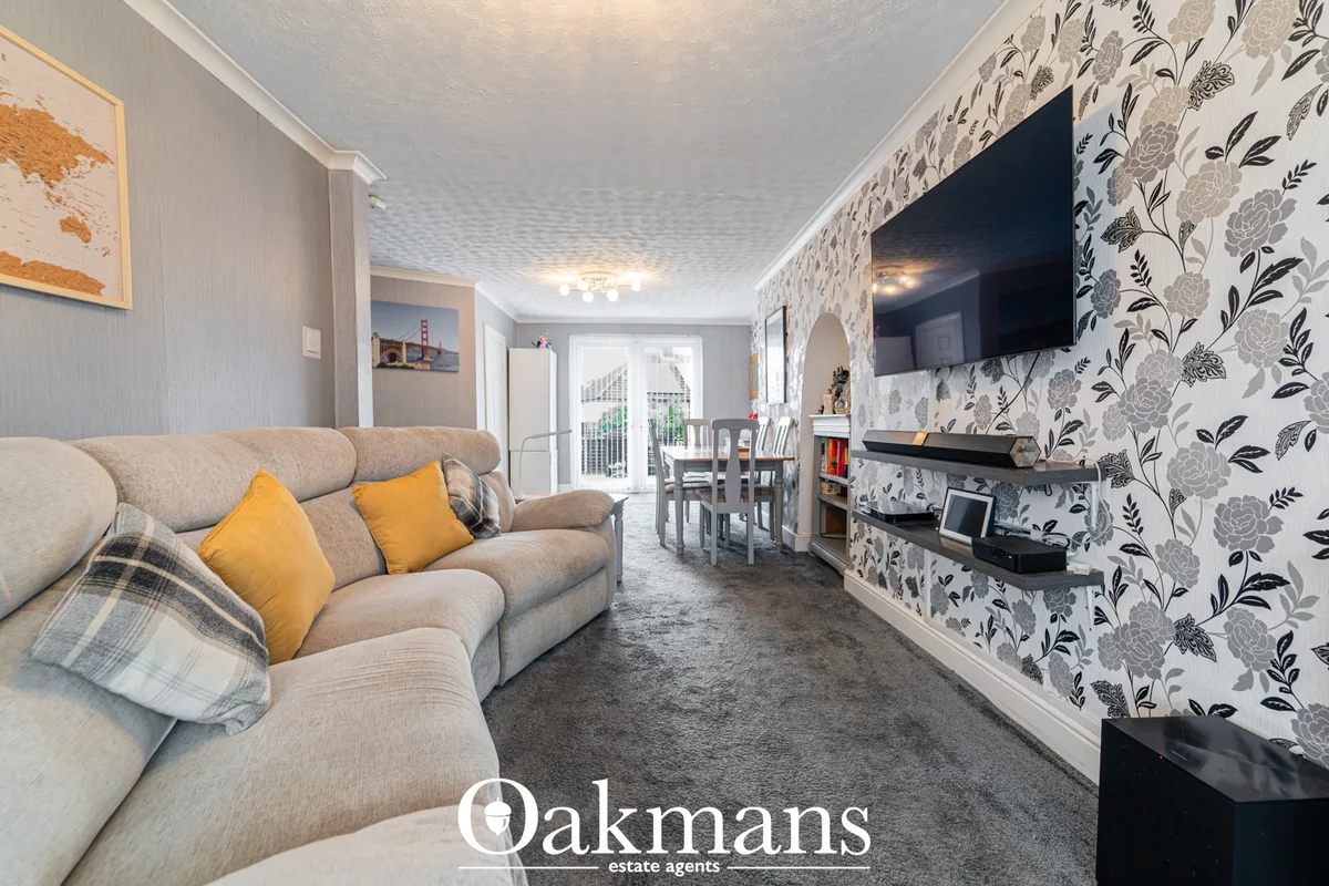 Open-plan living room with beige sofa, yellow cushions, floral wallpaper accent wall, wall-mounted TV, and view through 