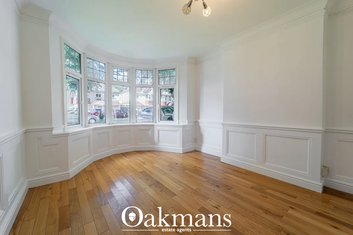 Bright living room with curved bay window, white panelled walls, wooden flooring and pendant lighting