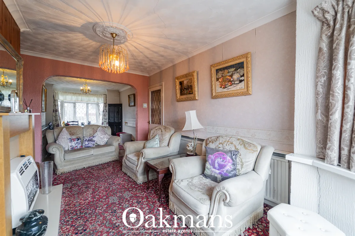 Traditional living room with cream upholstered furniture, ornate gold-framed artwork, red patterned carpet, decorative c
