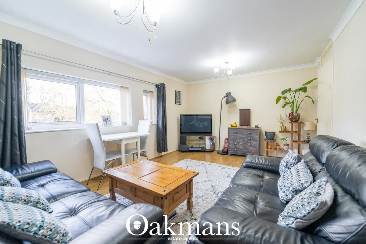 Spacious living room with black leather sofa, wooden coffee table, flat-screen TV, dining area with white chairs, potted