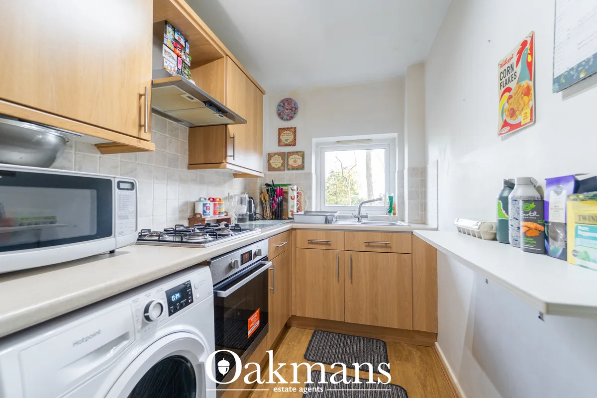Modern fitted kitchen with wooden cabinetry, white worktops, gas hob, integrated appliances and window overlooking garde