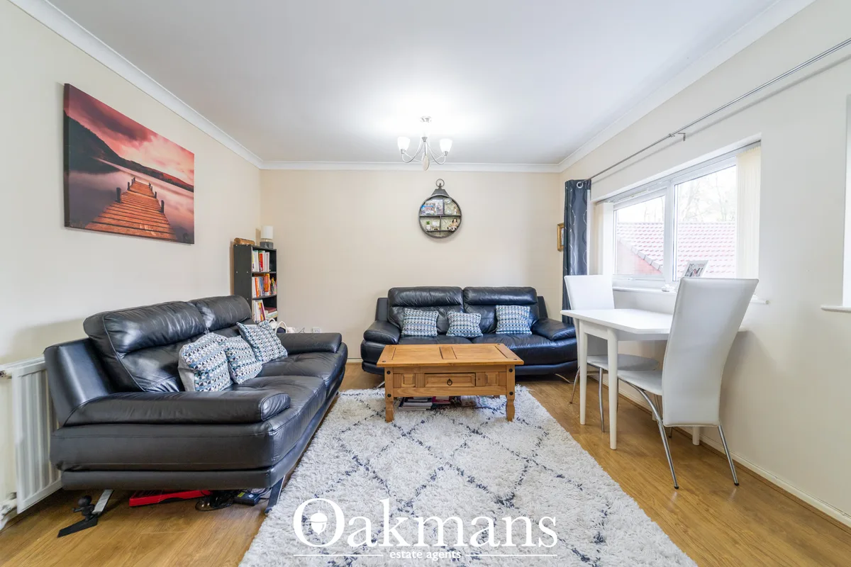 Spacious living room with black leather sofas, wooden coffee table, patterned rug, desk area, bookshelf, and large windo