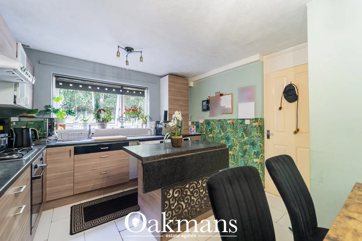 Modern fitted kitchen with wooden cabinetry, dark granite worktops, breakfast bar, and feature wallpaper wall. Large win