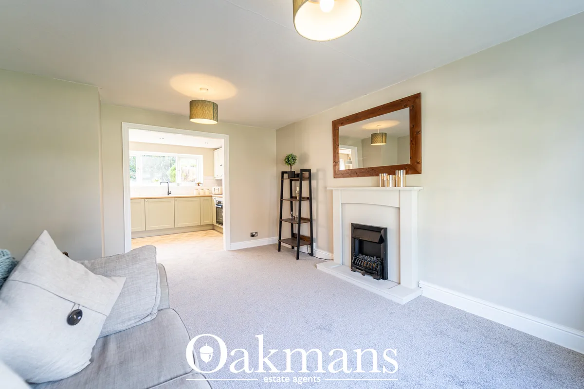 Bright living room with cream carpet, fireplace with wooden-framed mirror above mantelpiece, cream sofa, and open-plan k