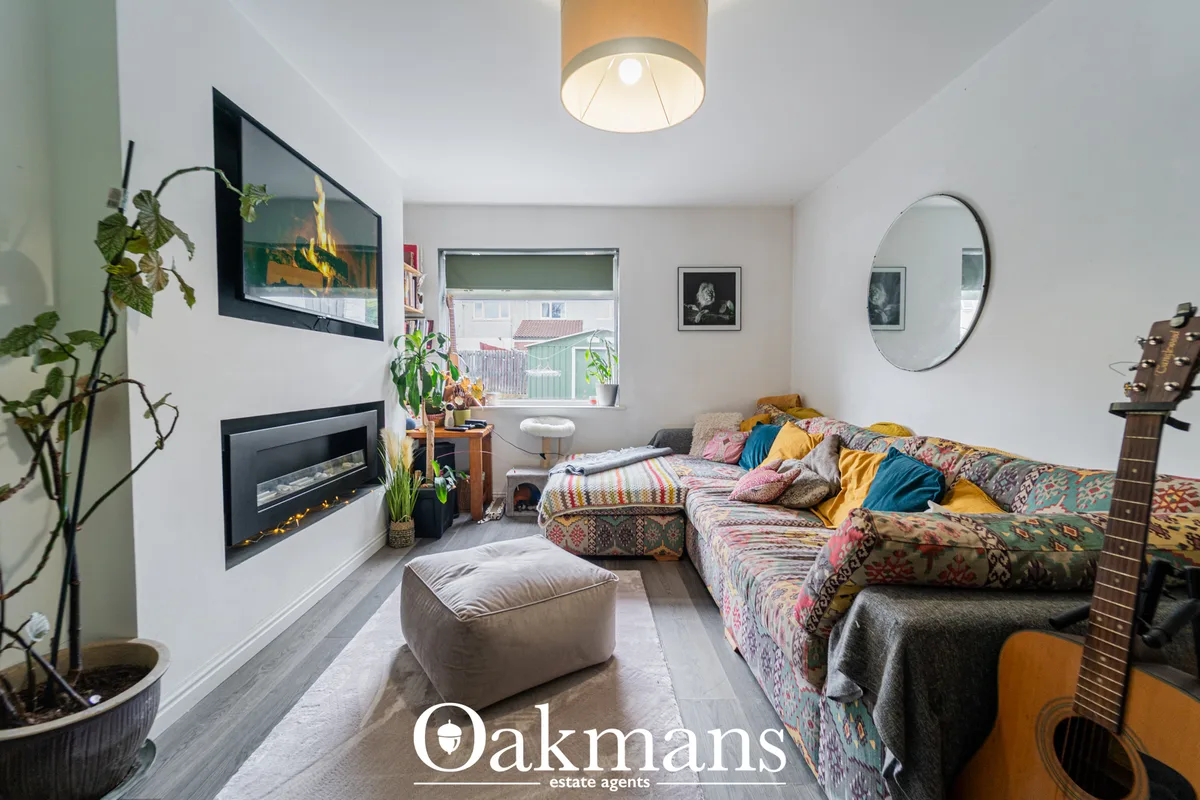 Bright living room with fireplace, colorful patterned sofa, round mirror, potted plants, guitar, and window with street 