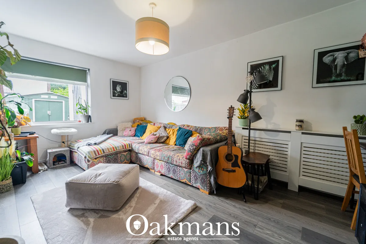 Bright living room with colorful patterned sofa, beige pouffe, wooden guitar, pendant lighting, framed wildlife artwork 