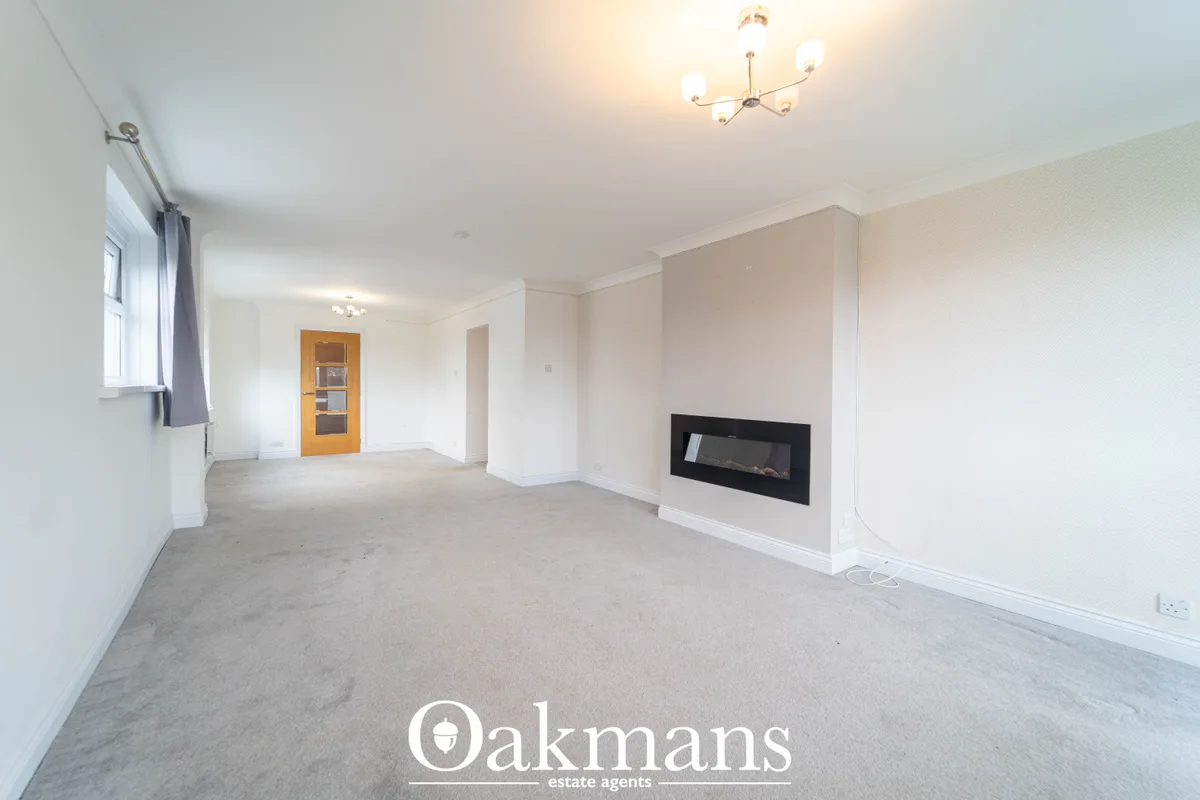 Spacious living room with neutral decor, carpet flooring, wall-mounted electric fireplace, wooden door with glass panels