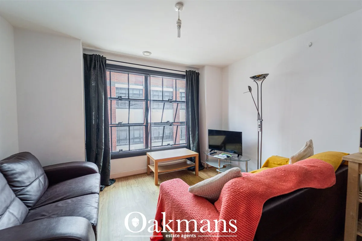 Spacious living room with dark leather sofas, red throw blanket, wooden coffee table, flat-screen TV, floor lamp, and la
