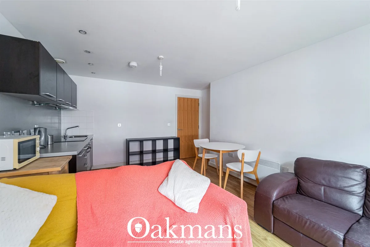 Open-plan living space with burgundy leather sofa, round dining table with wooden chairs, fitted kitchen with black unit