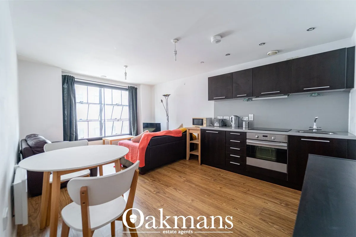 Open-plan living room and kitchen with black fitted units, wooden dining table, sofa, large windows with blue curtains a