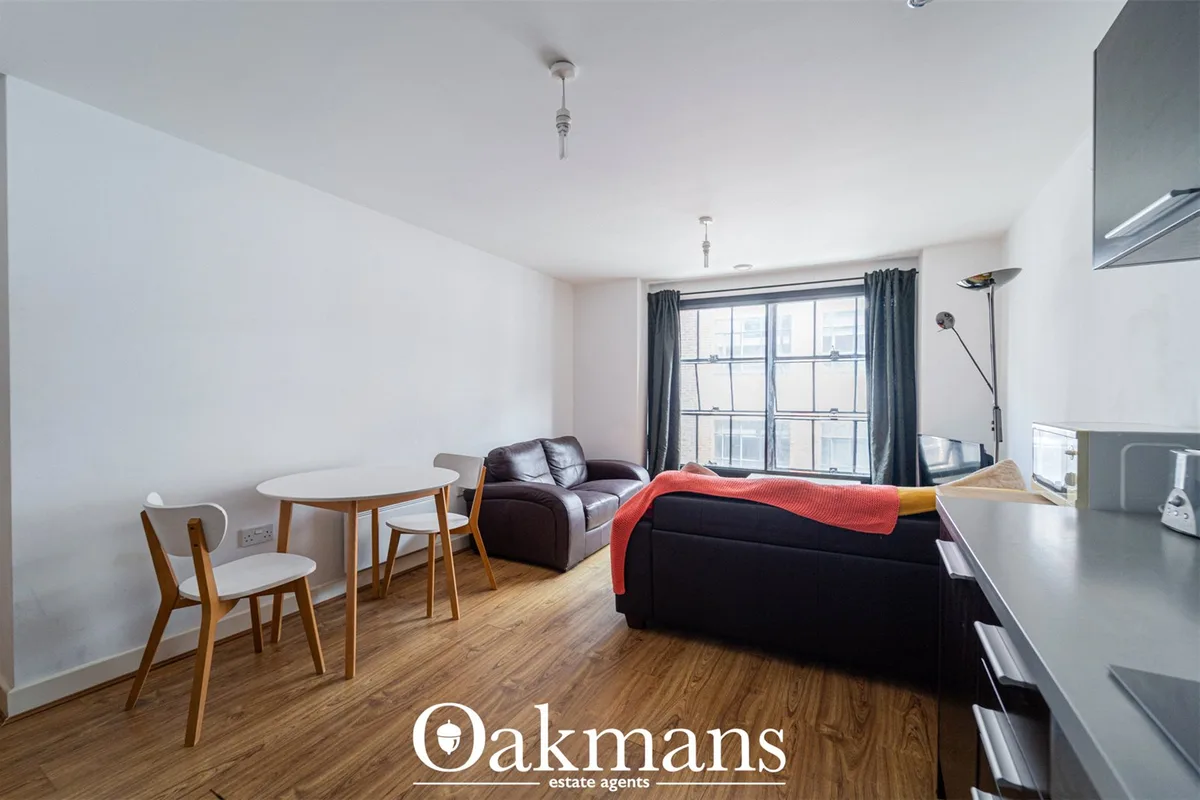 Open-plan living area with black leather sofa, dining table with wooden chairs, large window with grey curtains, wooden 