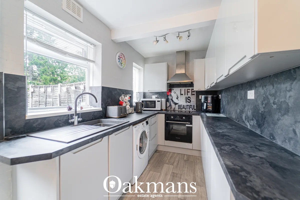 Modern galley kitchen with white units, dark slate worktops, black appliances, washing machine and window overlooking ga
