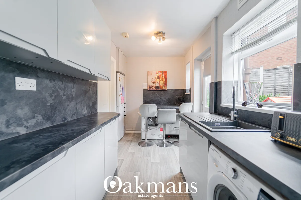 Modern galley kitchen with white units, dark slate worktops, stainless steel sink, integrated appliances, and breakfast 