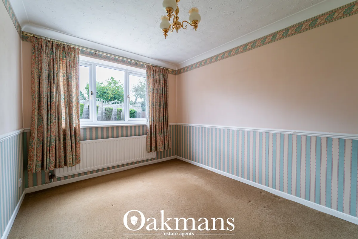 Empty bedroom with cream and blue striped wallpaper, radiator, patterned curtains, white ceiling and small chandelier