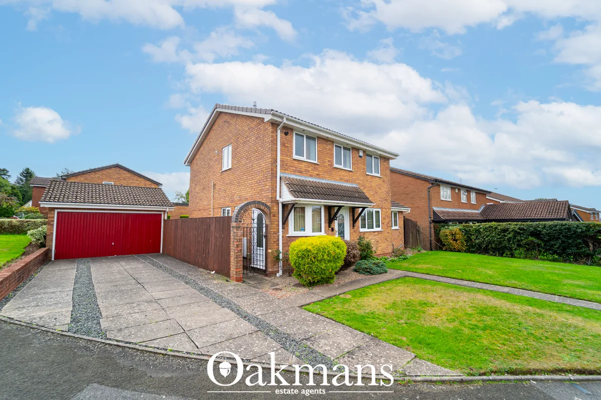 Brick-built detached house with red garage door, driveway, manicured front garden and hedging under clear sky