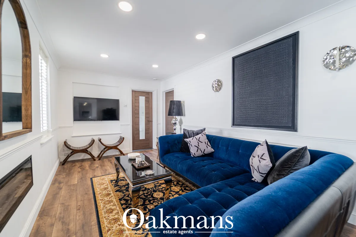 Modern living room with blue sectional sofa, wall-mounted TV, fireplace, wooden flooring, decorative clock and large win
