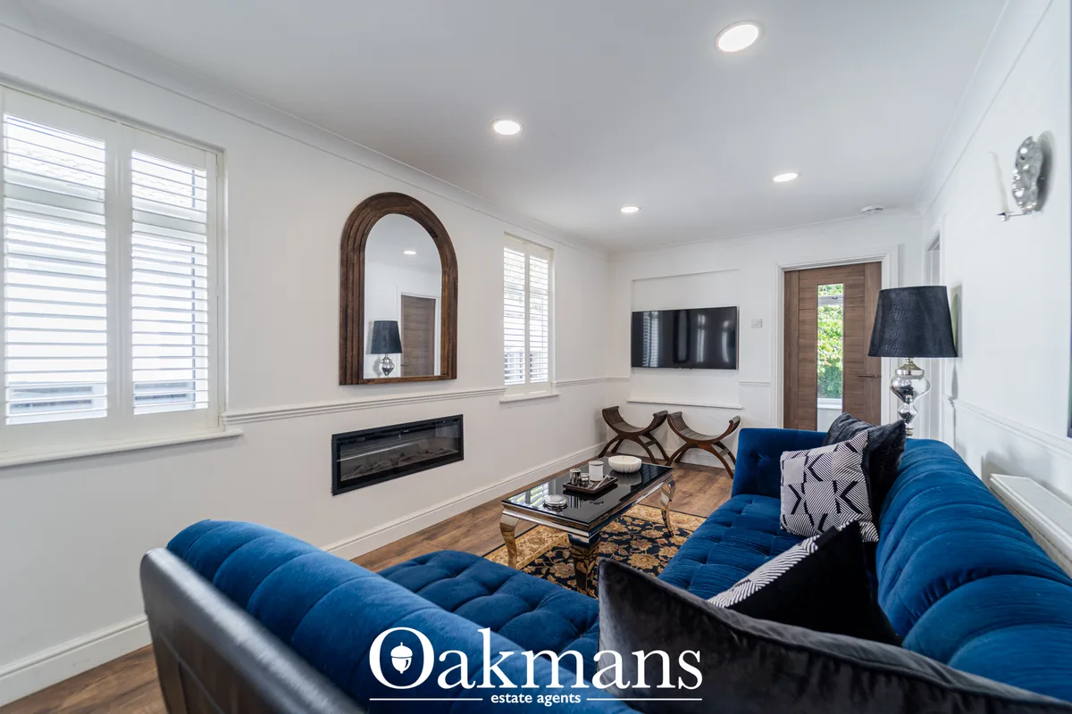 Modern living room with dual blue sofas, wooden-framed mirror, flat-screen TV, fireplace, wood flooring, and recessed li