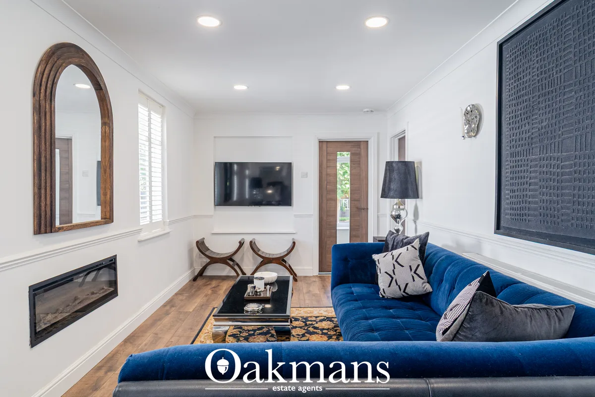 Modern living room with blue velvet sectional sofa, wall-mounted TV, fireplace, wooden-framed mirror, recessed lighting 