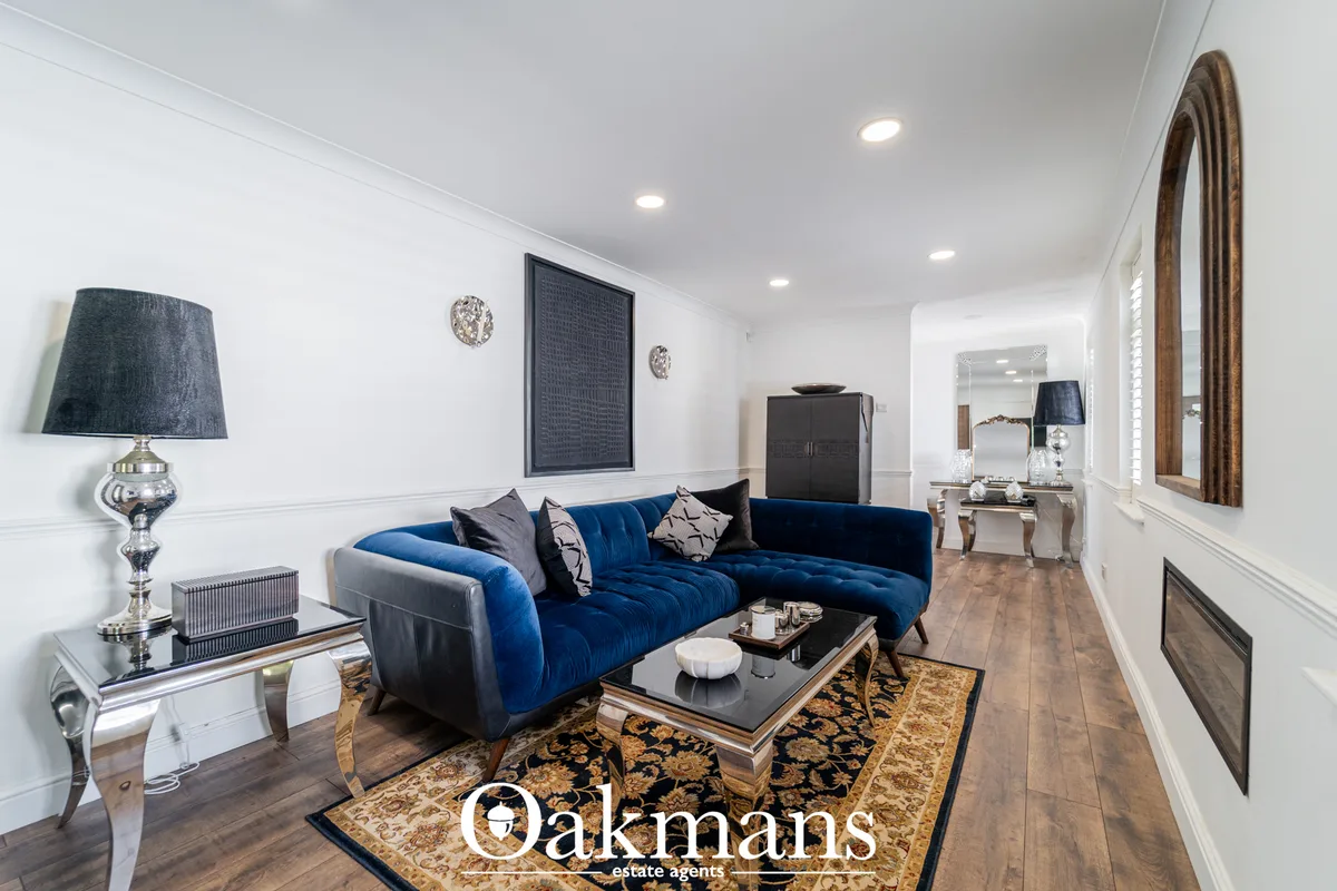 Modern living room with blue velvet sofa, decorative pillows, glass coffee table on patterned rug, wall art, recessed li