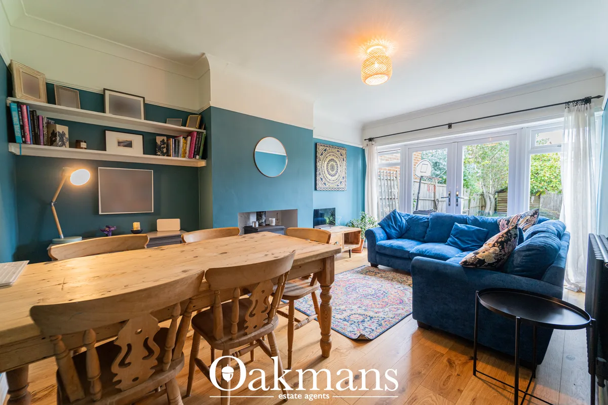 Open-plan living and dining space with blue velvet sofa, wooden dining table, teal accent wall, built-in shelving, and g