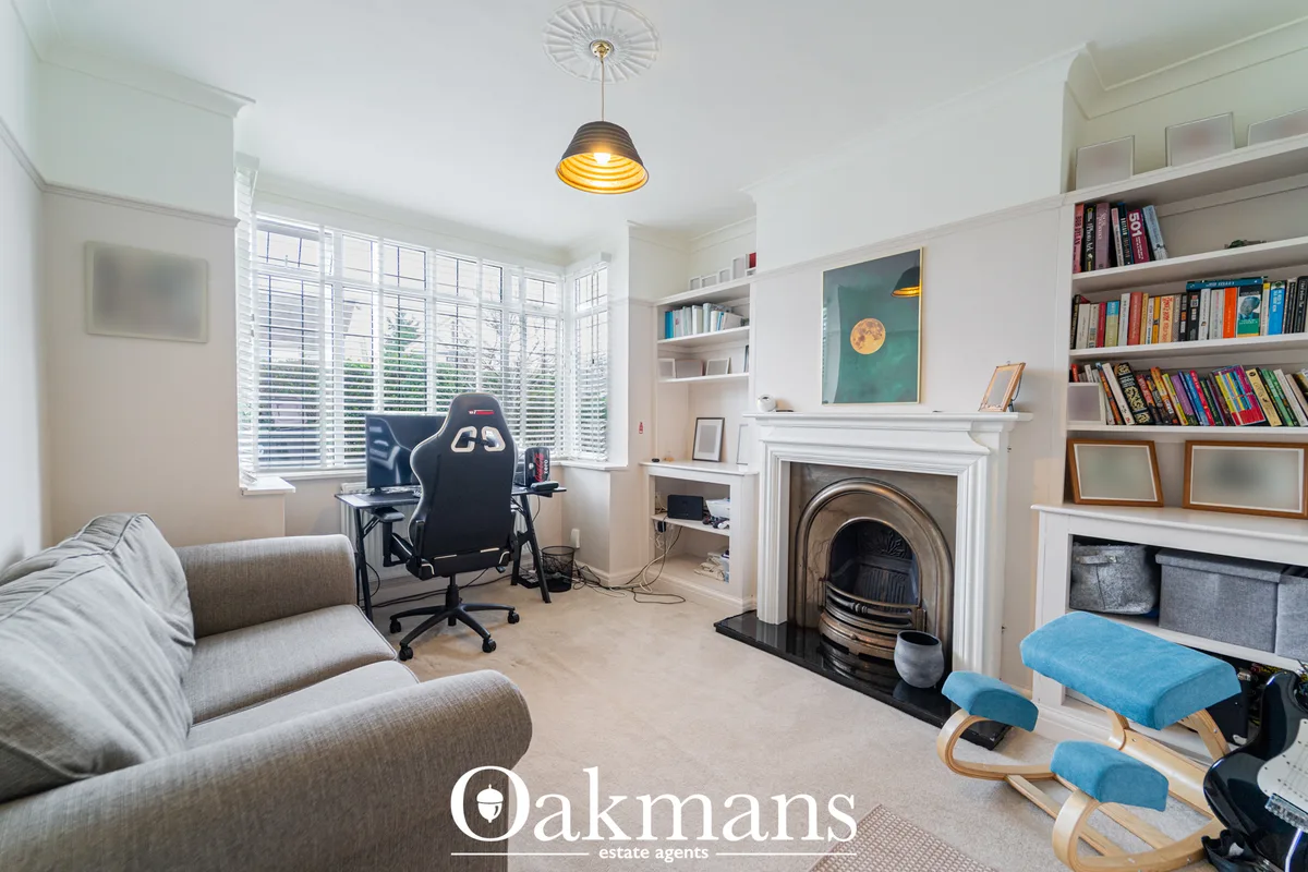 Bright study with gaming chair, desk, built-in bookshelves, fireplace, sofa and large shuttered windows