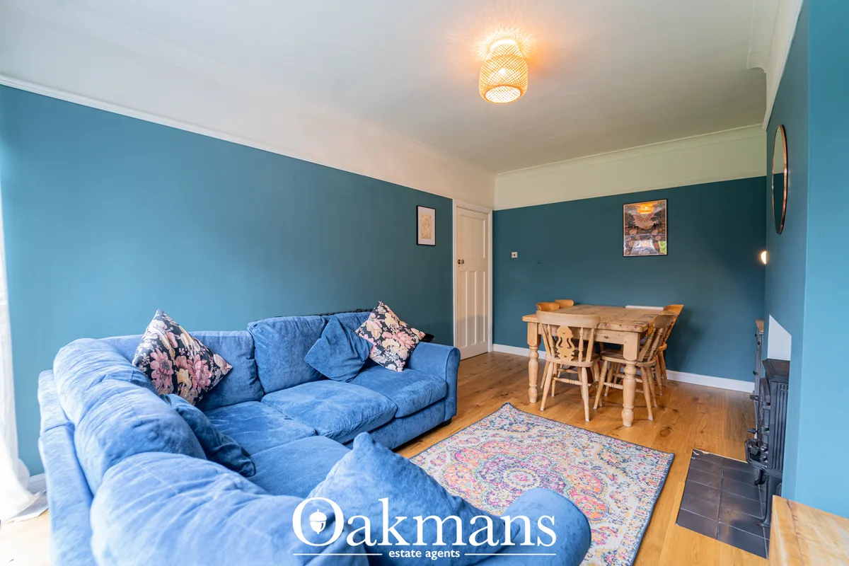 Open-plan living and dining room with blue corner sofa, wooden dining table, colorful rug, teal feature wall and ceiling