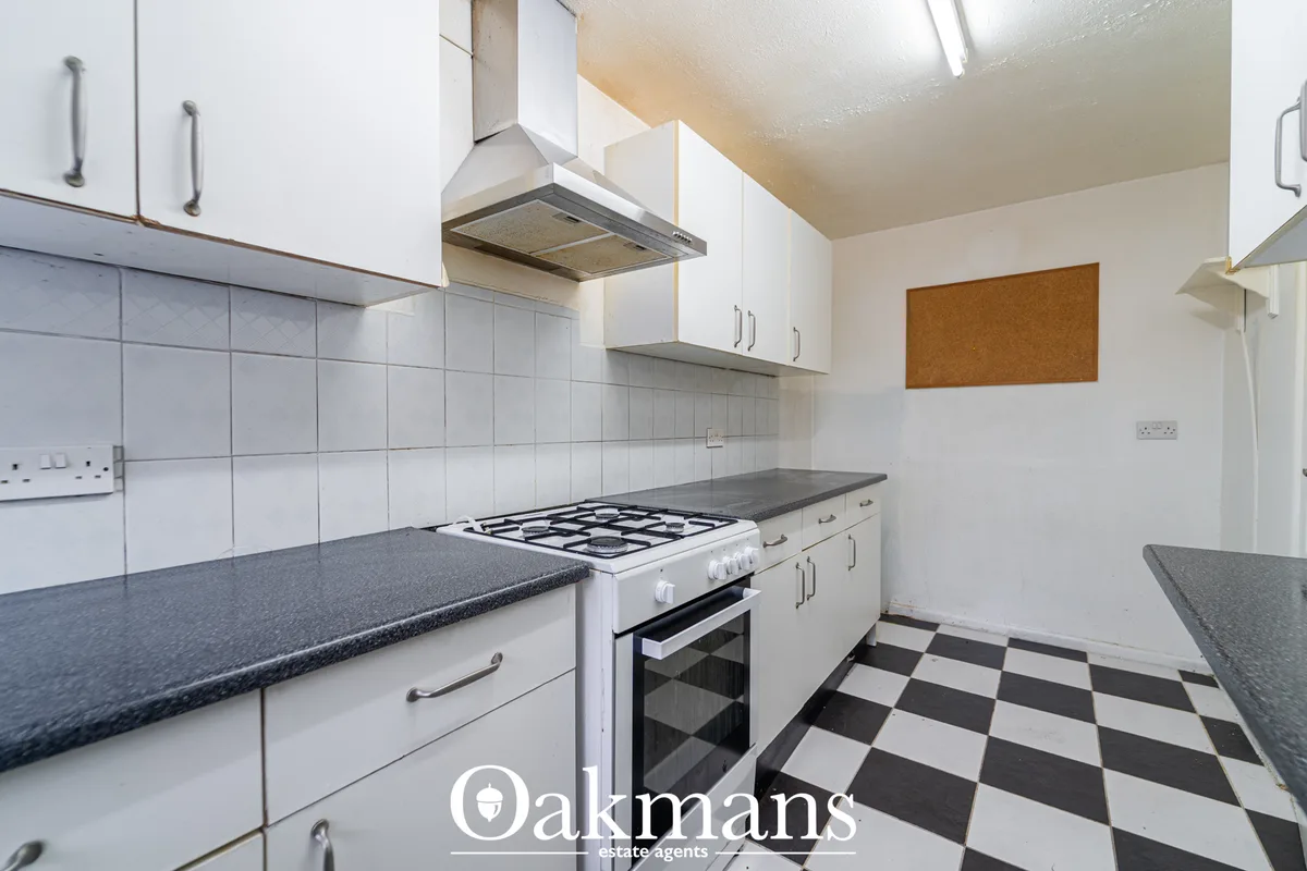 White fitted kitchen with gas cooker, granite worktops, tiled splashback, wall-mounted extractor hood and black-and-whit