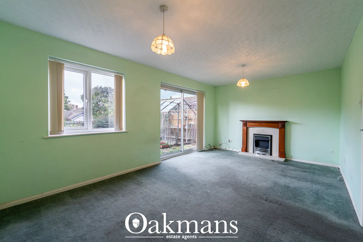 Spacious living room with lime green walls, grey carpet, fireplace with wood surround, two pendant lights, large windows