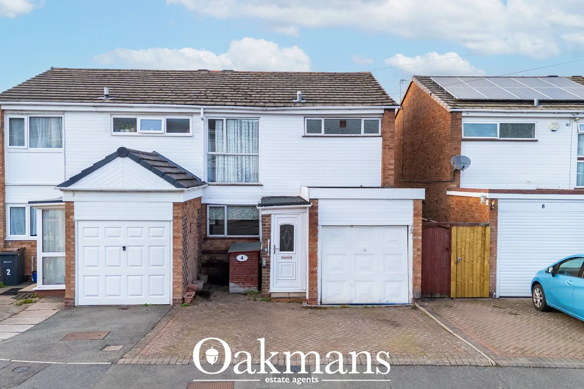 Row of terraced houses with white render, red brick chimneys, garage doors, brick driveways and parked cars in bright da