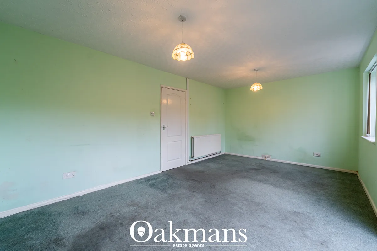 Spacious living room with pale green walls, grey carpet, two pendant lights, white door and window with natural light