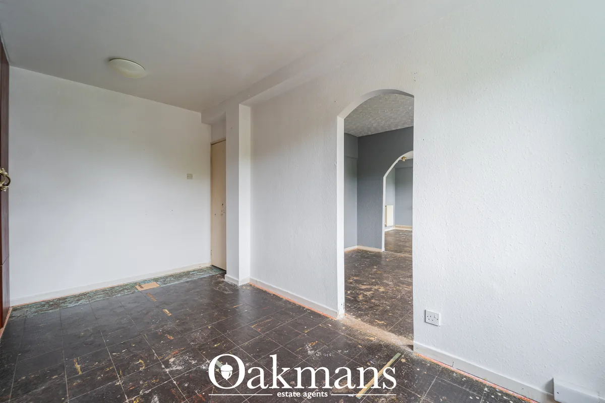 Bright white hallway with dark tiled flooring, white walls, arched doorway to adjacent room, and recessed ceiling light