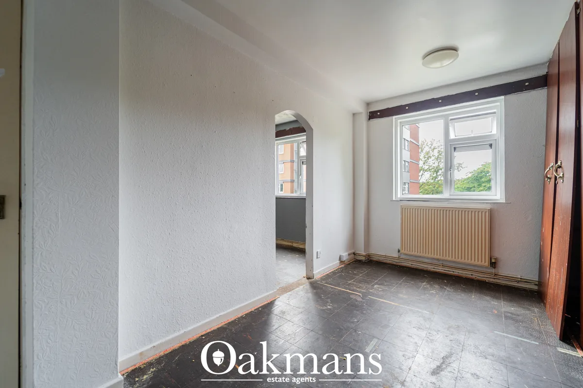 Bright hallway with white walls, dark tile flooring, radiator, window with urban views, and wooden wardrobe door
