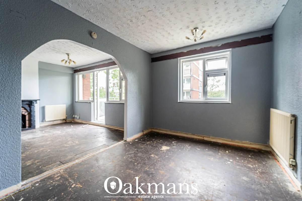 Spacious living room with grey walls, textured ceiling, arched doorway to adjoining room, radiators, windows with exteri