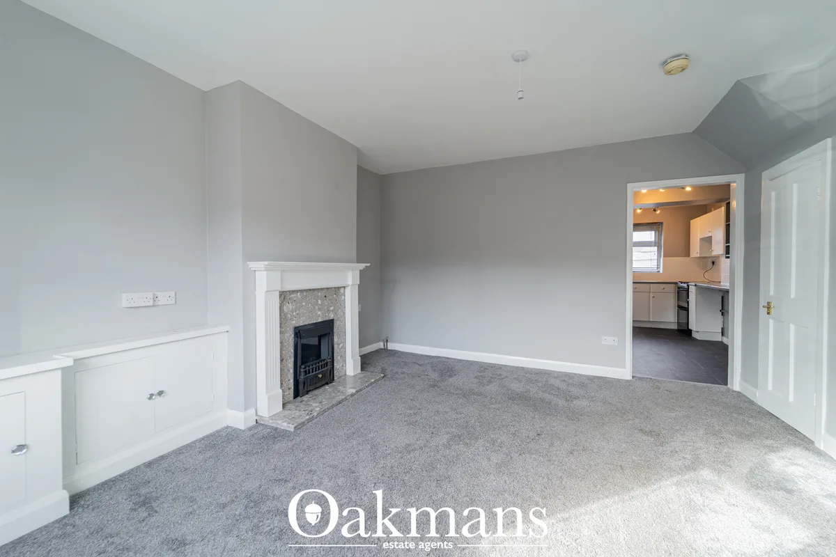Spacious living room with grey carpet, white fireplace with black insert, white wainscoting, grey walls, recessed lighti
