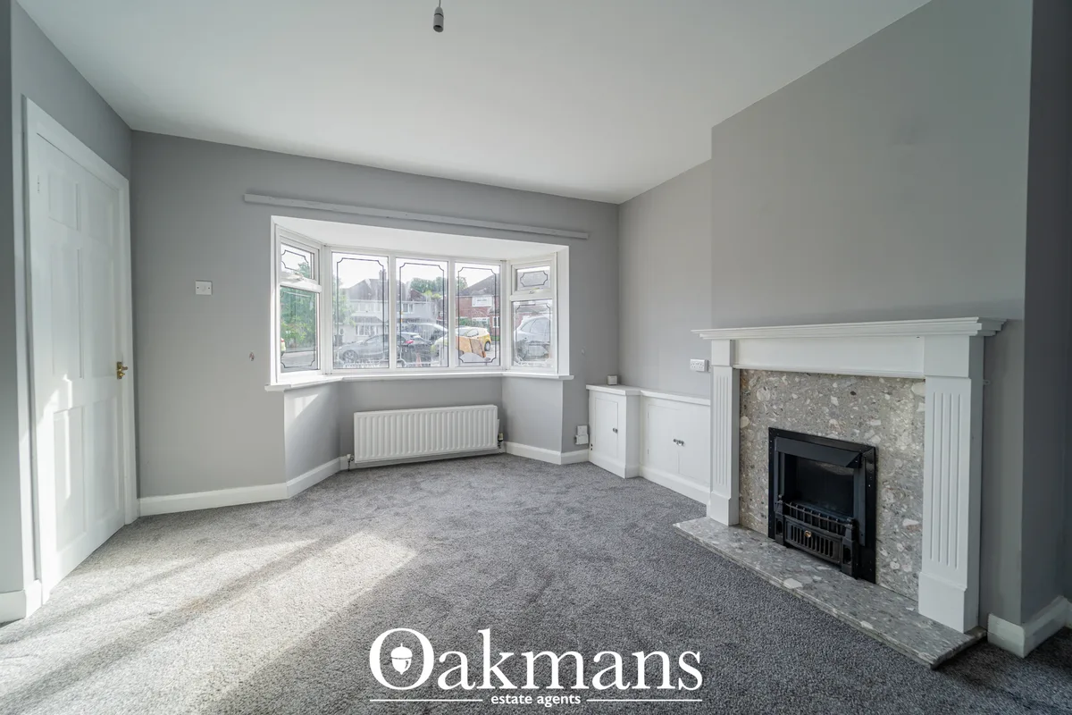 Bright living room with gray walls, bay window, fireplace with stone surround, white mantelpiece, radiator, and gray car