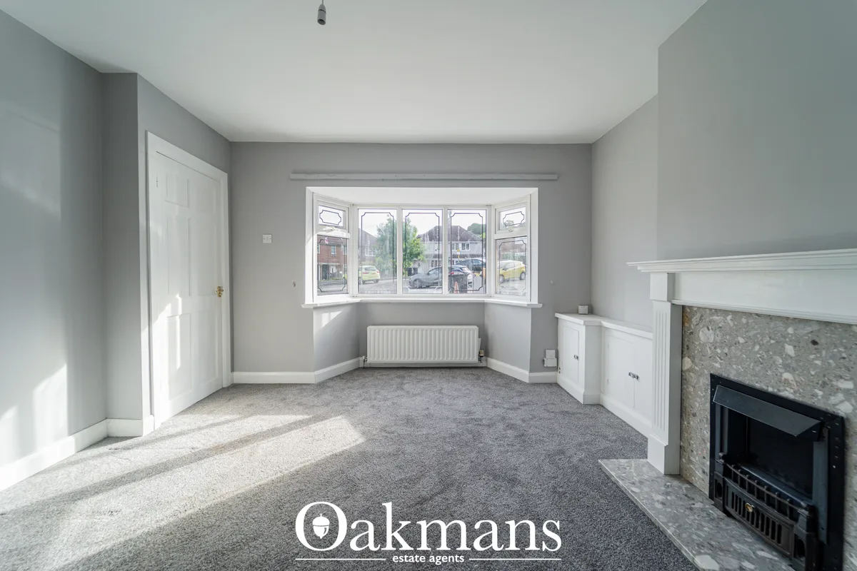 Bright living room with bay window overlooking street, fireplace with stone surround, white woodwork, gray walls and gra