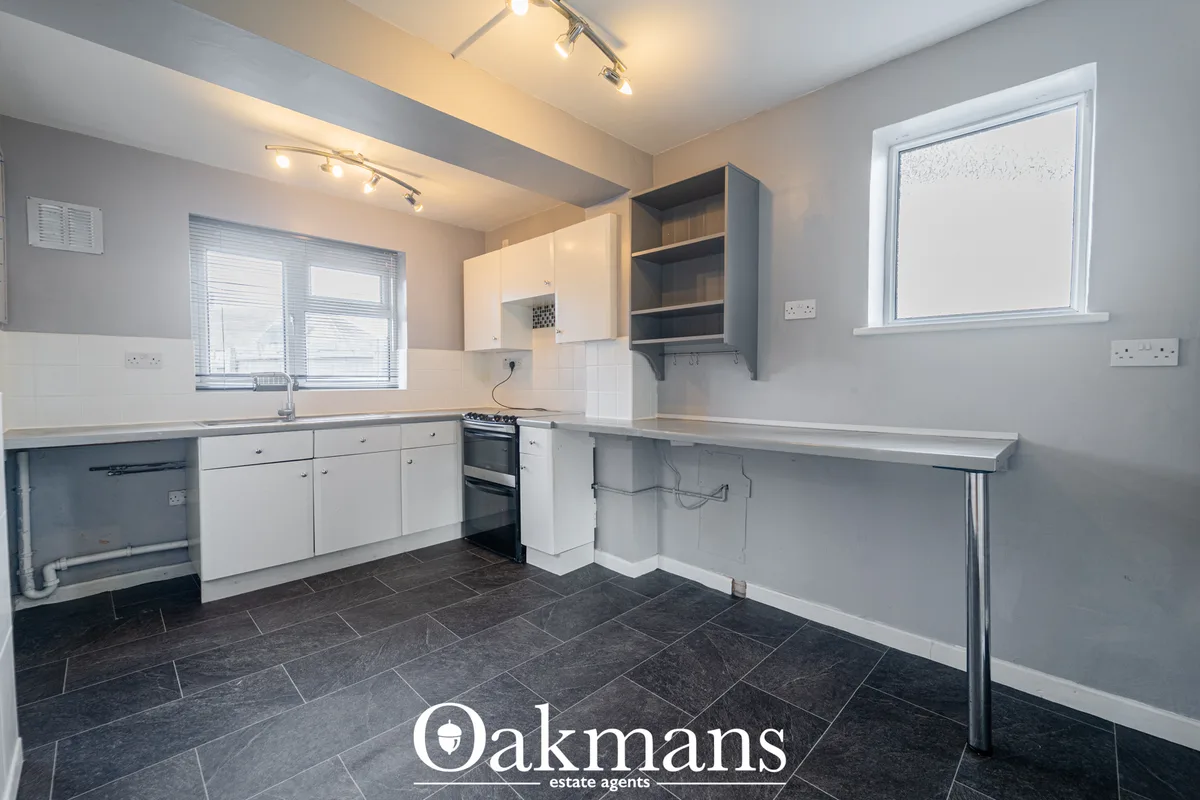 Modern fitted kitchen with white units, stainless steel double oven, dark tile flooring, breakfast bar and dual windows