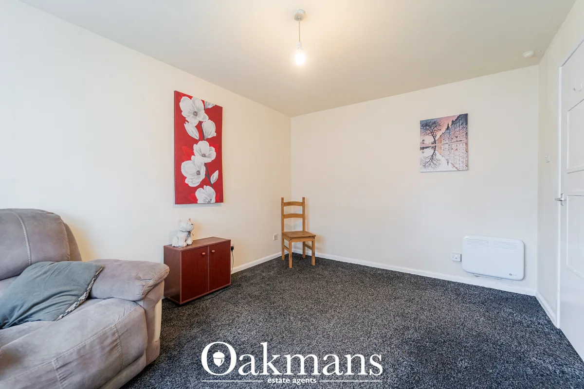 Spacious living room with cream walls, dark carpet, grey armchair, wooden chair, red cabinet with white flower artwork a
