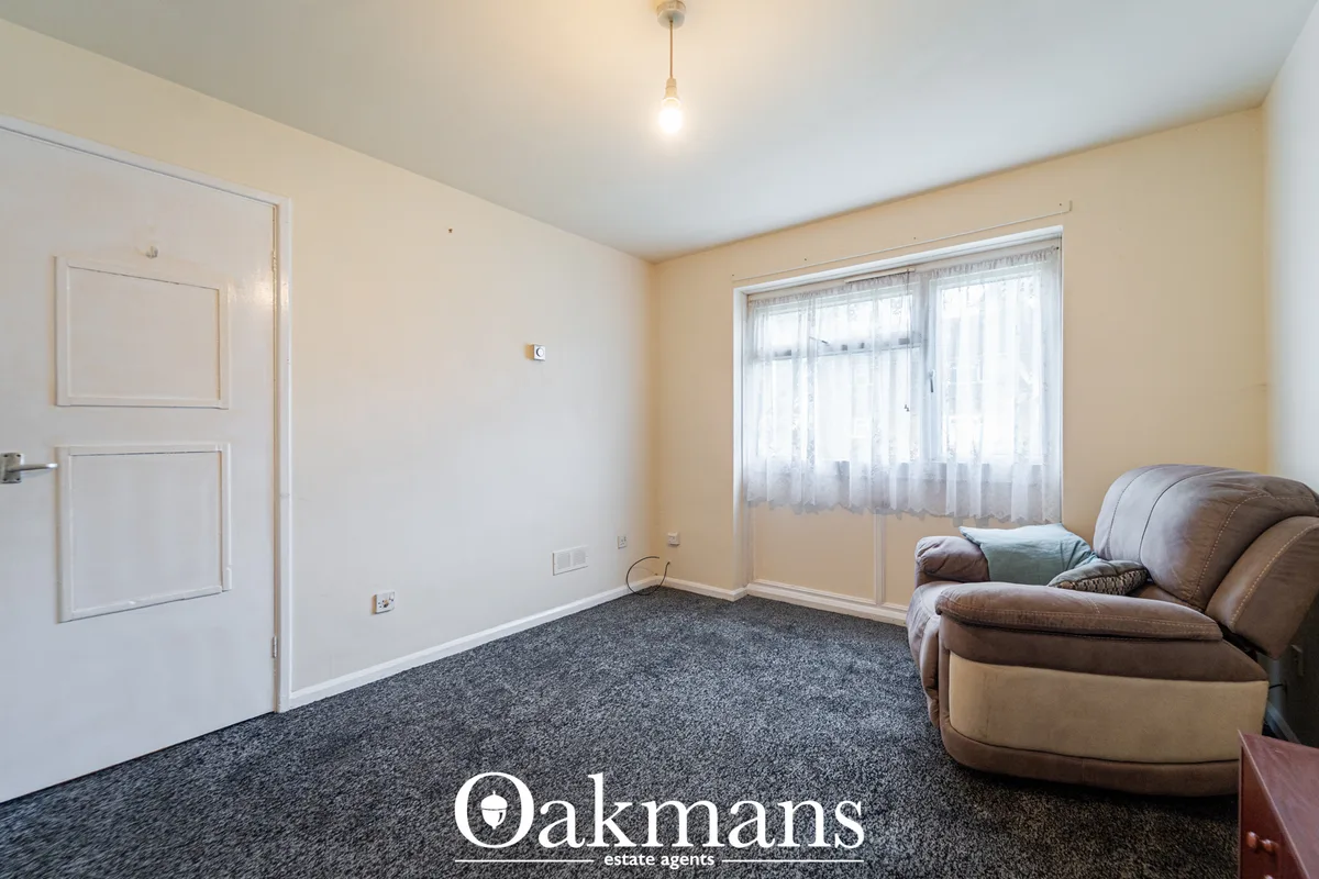 Spacious living room with grey carpet, cream walls, brown leather armchair, patio doors with sheer curtains and pendant 