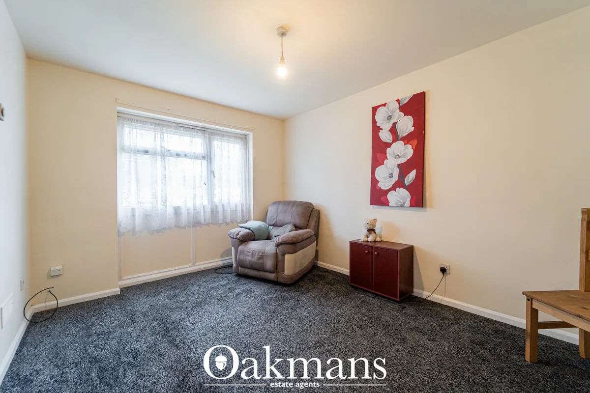 Spacious living room with beige walls, grey carpet, recliner armchair, wooden furniture, red floral artwork, large windo