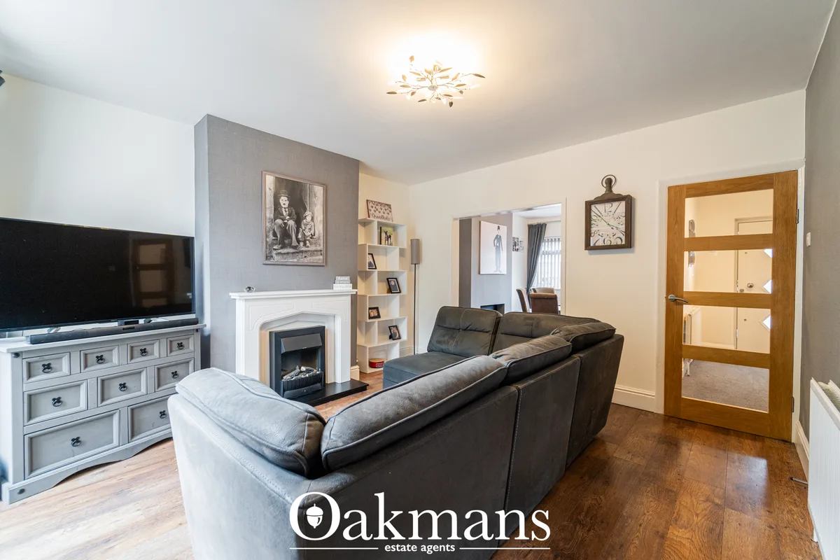 Spacious living room with dark leather sofa, fireplace with white surround, flat-screen TV, wooden flooring and neutral 