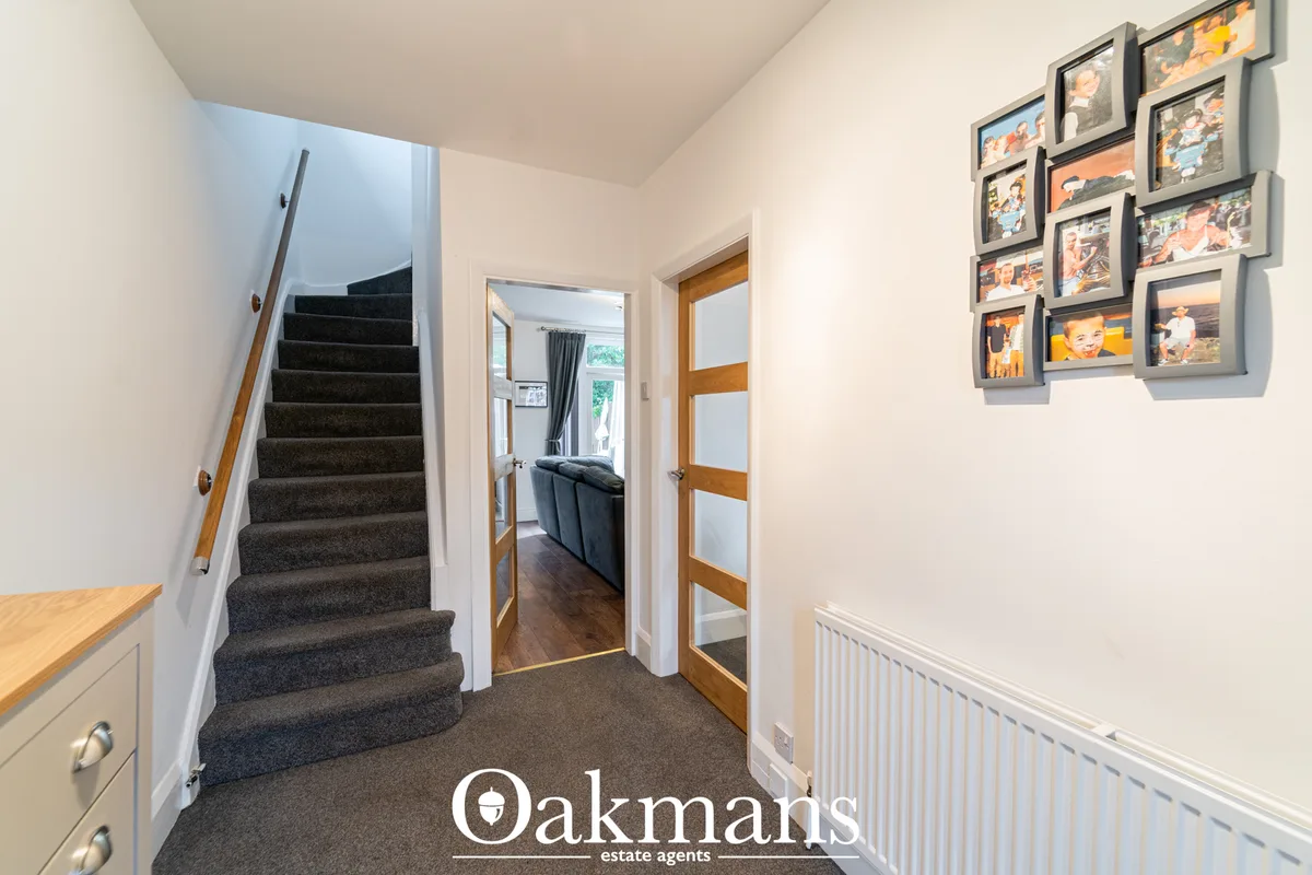 Bright hallway with dark staircase, wooden doors, white walls, radiator, and family photo frames on wall