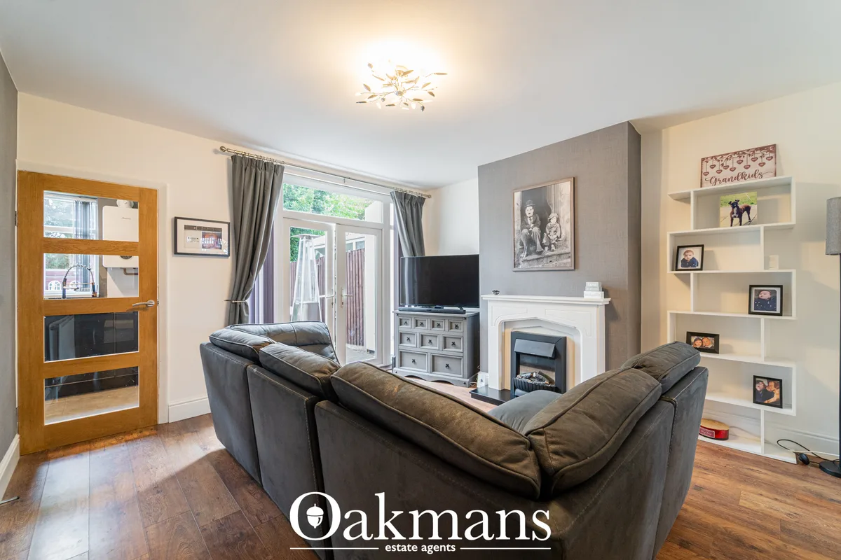 Spacious living room with dark leather corner sofa, white fireplace, TV on storage unit, built-in shelving with family p