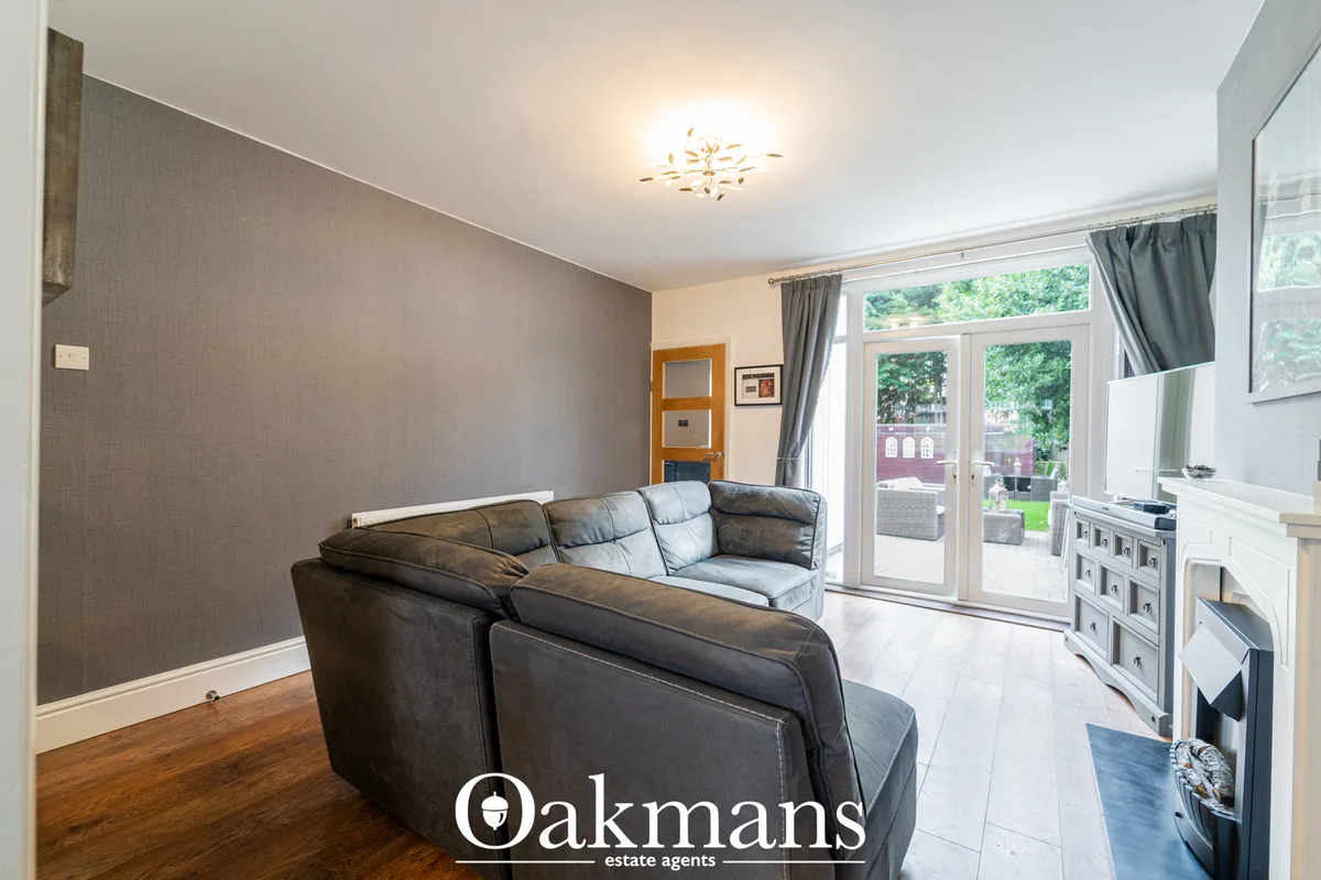 Open-plan living area with dark leather corner sofa, grey feature wall, wooden flooring, ceiling light fixture, patio do