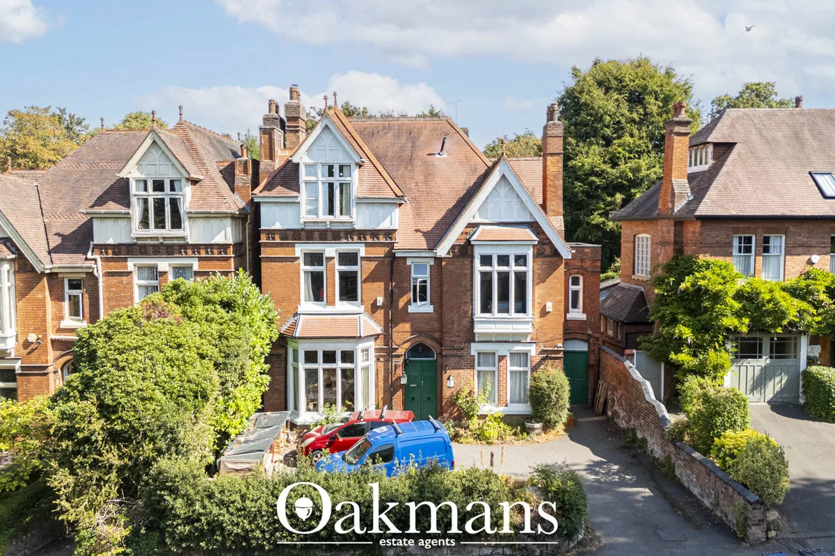 Aerial view of red-brick Victorian and Edwardian homes with slate roofs, white bay windows, chimneys and mature green tr